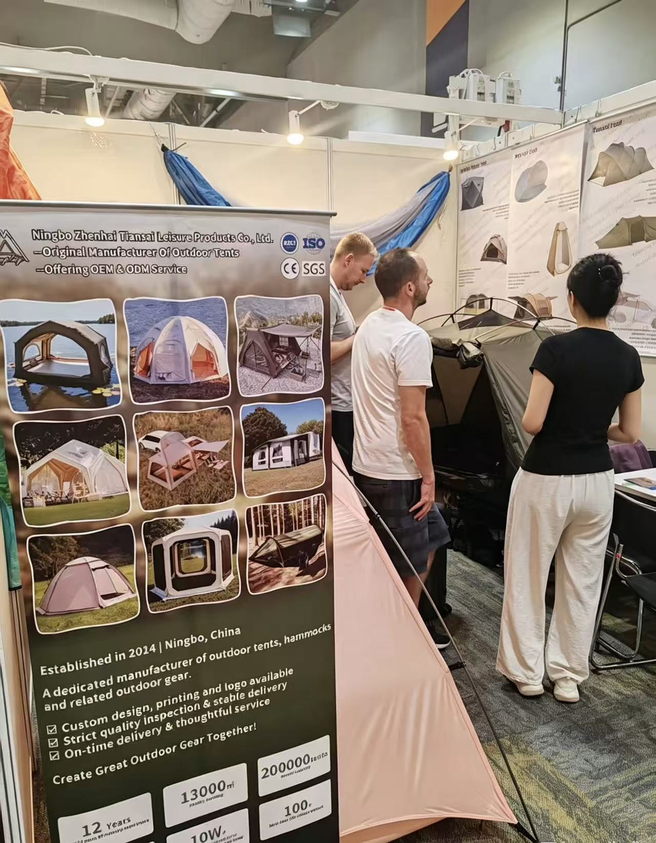 Visitors and a Tenplay team member speaking beside product posters and tent samples